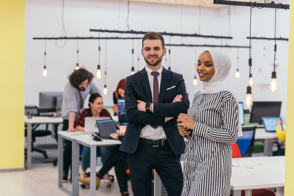 Portrait of a formal businessman and young African American businesswoman posing with their team in a modern startup office. Marketing concept. Multi-ethnic society.